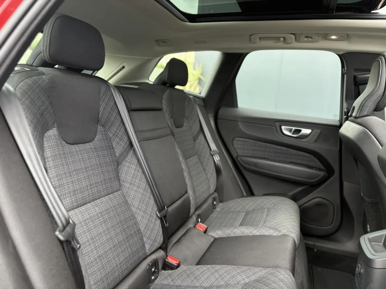 Vue latérale droite de l'intérieur arrière du Volvo XC60 2024, sièges en tissu gris à motif carreaux et ceintures noires.