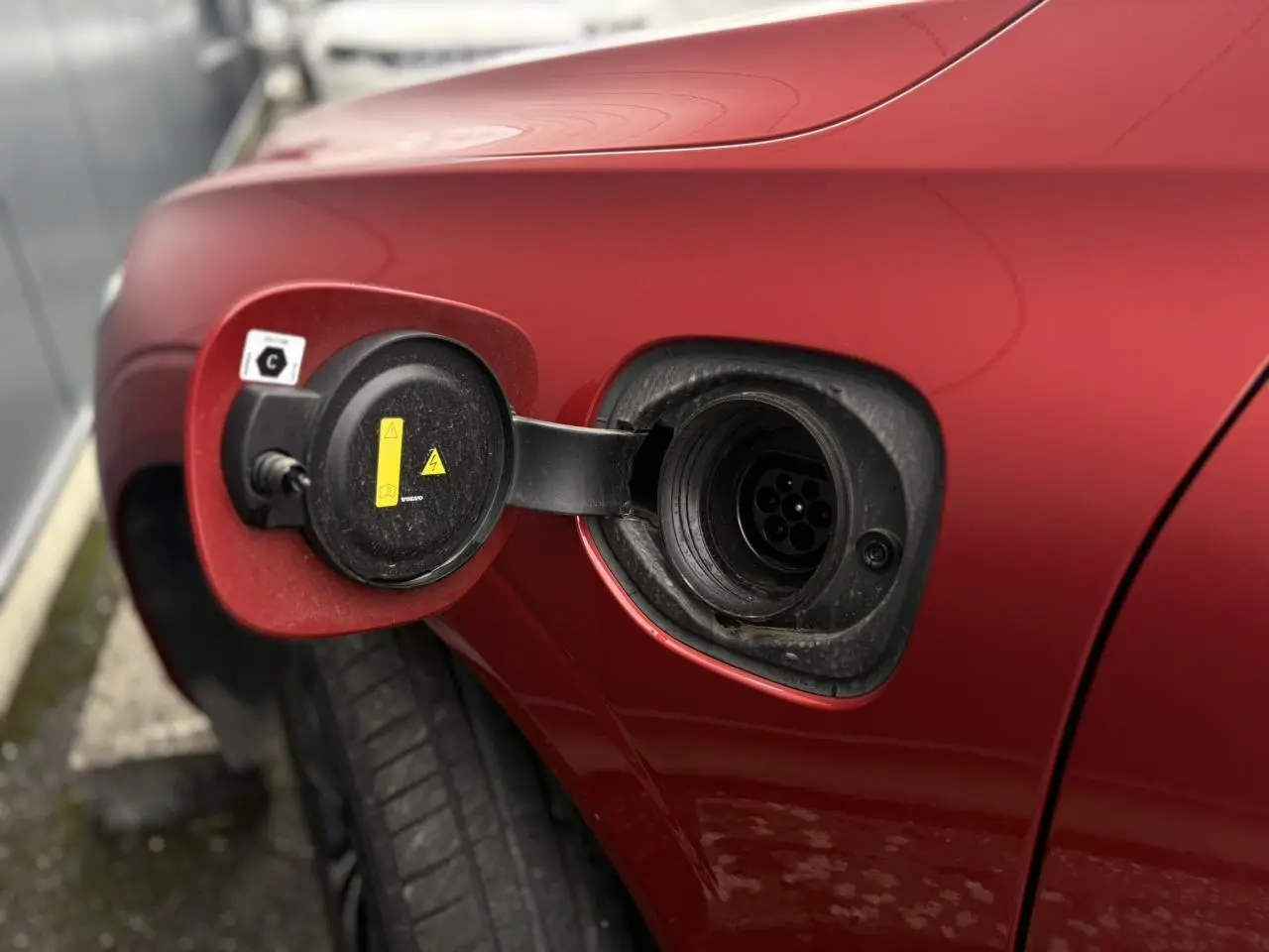 Prise de recharge ouverte côté gauche arrière d'un Volvo XC60 rouge fusion hybride rechargeable 2024.