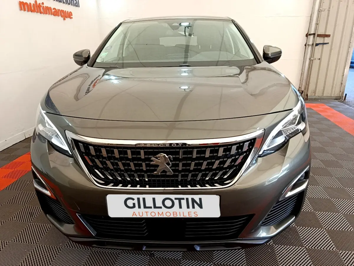 Vue frontale d'un Peugeot 3008 gris foncé avec calandre chromée et phares LED allumés dans un showroom.