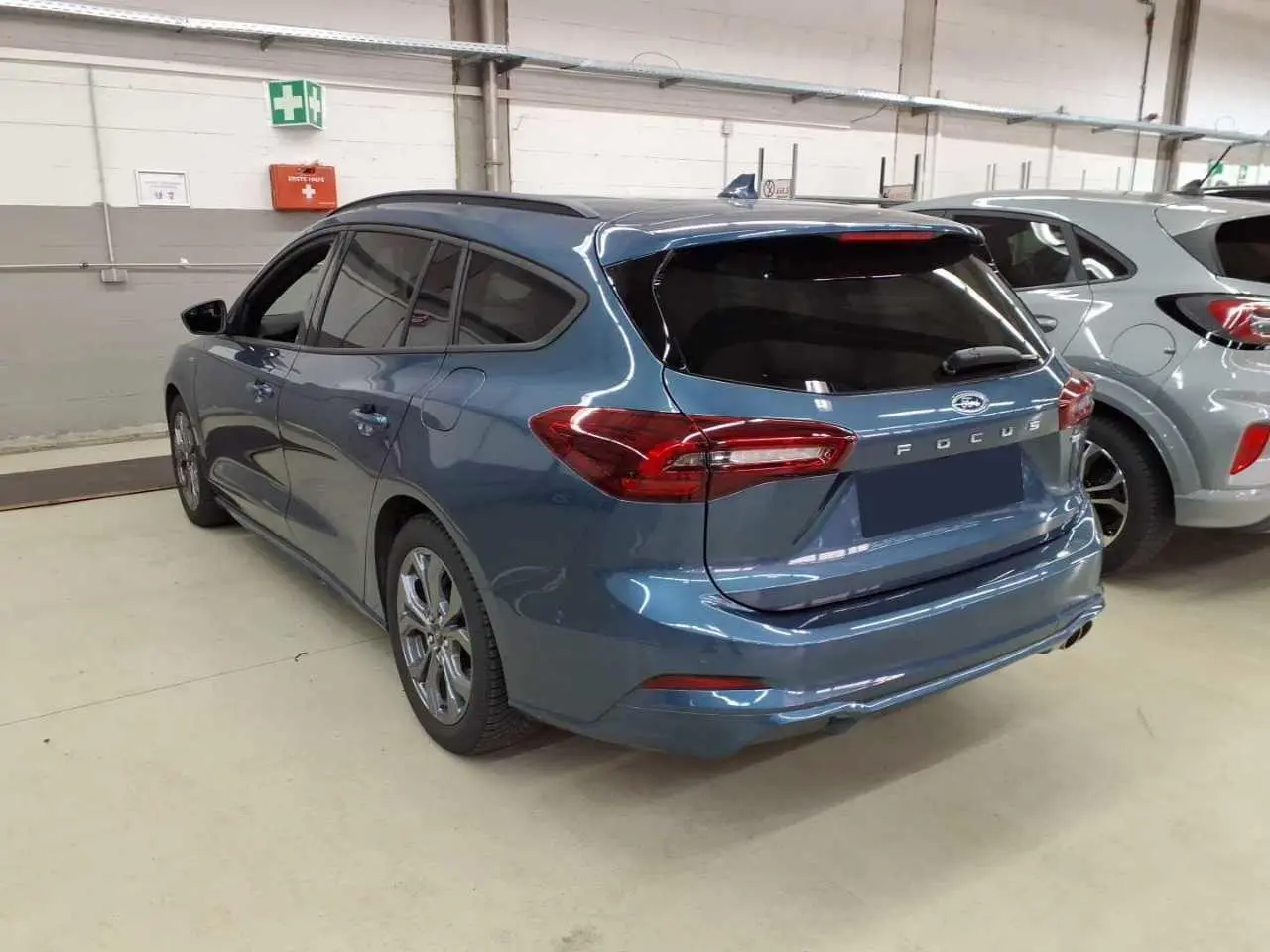 Vue 3/4 arrière droite d'une Ford Focus SW 2023 bleu azur avec attelage et vitres arrière surteintées en intérieur d'atelier.