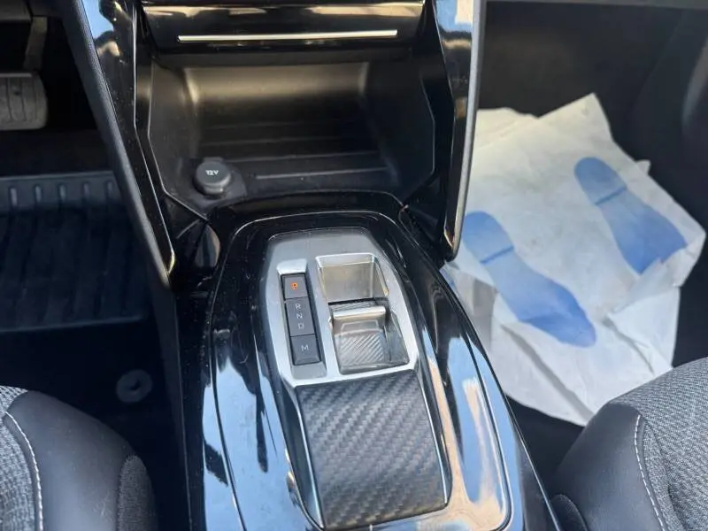 Gros plan sur la console centrale noire du Peugeot 2008 Hybrid 136 e-DCS6 Allure avec levier de boîte automatique et finition carbone.