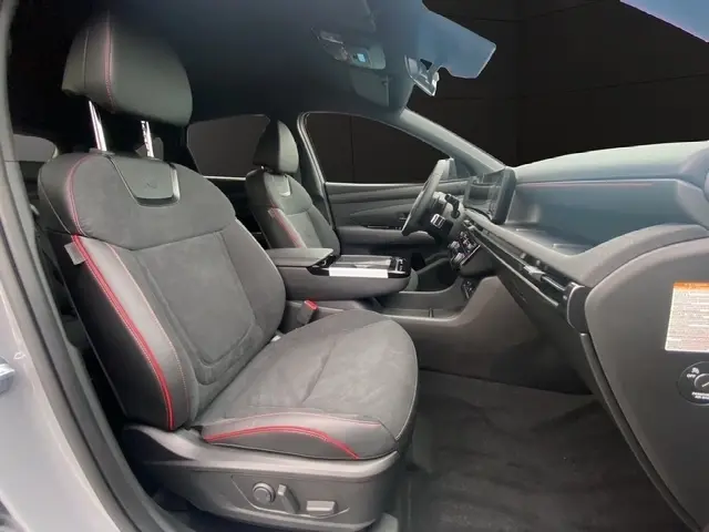 Vue intérieure côté conducteur du Hyundai Tucson gris foncé 2026, sièges noirs avec surpiqûres rouges et tableau de bord moderne.