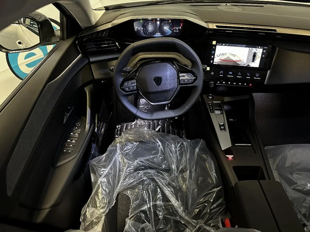 Vue intérieure avant centrée sur le volant compact et le tableau de bord numérique de la Peugeot 308 2024 blanc okenite.