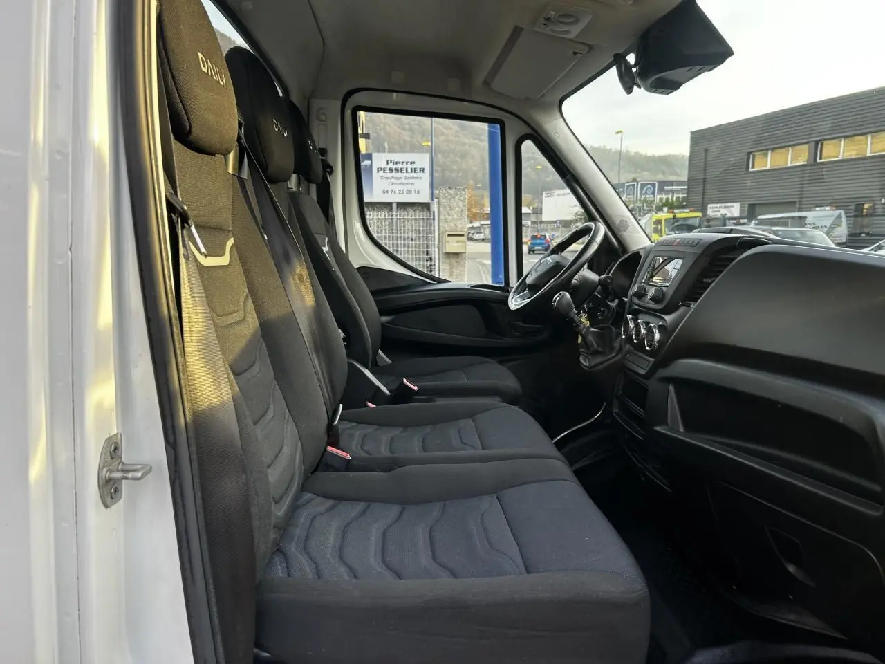 Intérieur du Iveco Daily blanc vu côté gauche, montrant les sièges noirs et le tableau de bord avec volant et levier de vitesses.