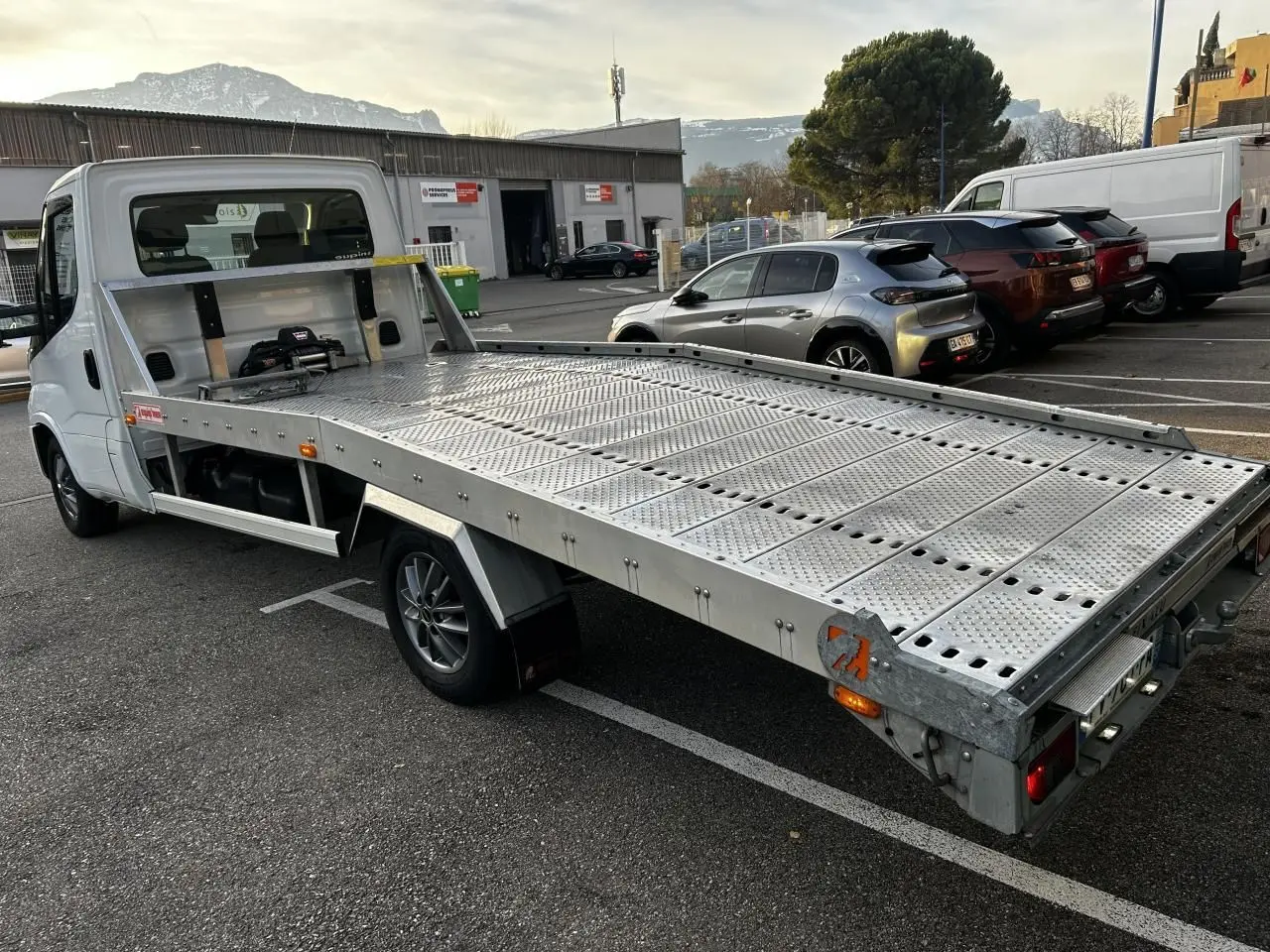 IVECO Daily blanc vu en 3/4 arrière côté gauche avec plateau métallique perforé et cabine simple.