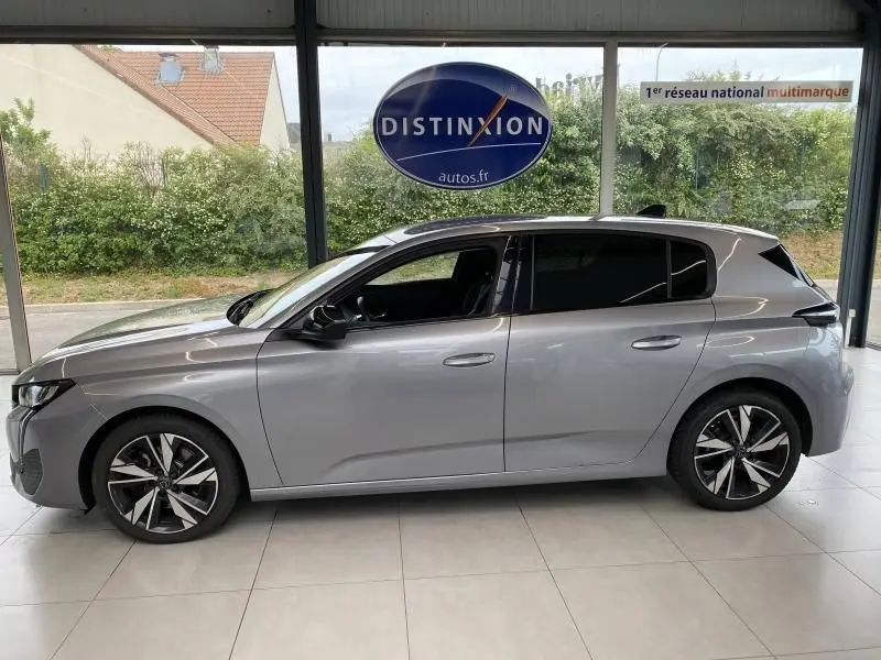 Peugeot 308 gris Artense vue de profil côté gauche, avec jantes alliage et vitres teintées en intérieur showroom.