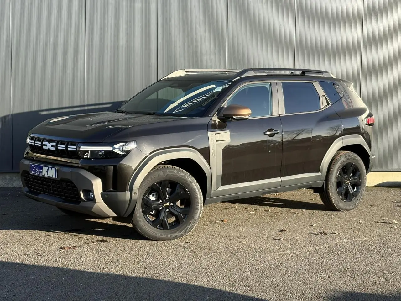 Dacia Duster 2026 noir nacré en 3/4 avant droit avec jantes noires et coques de rétroviseur brun cuivré.