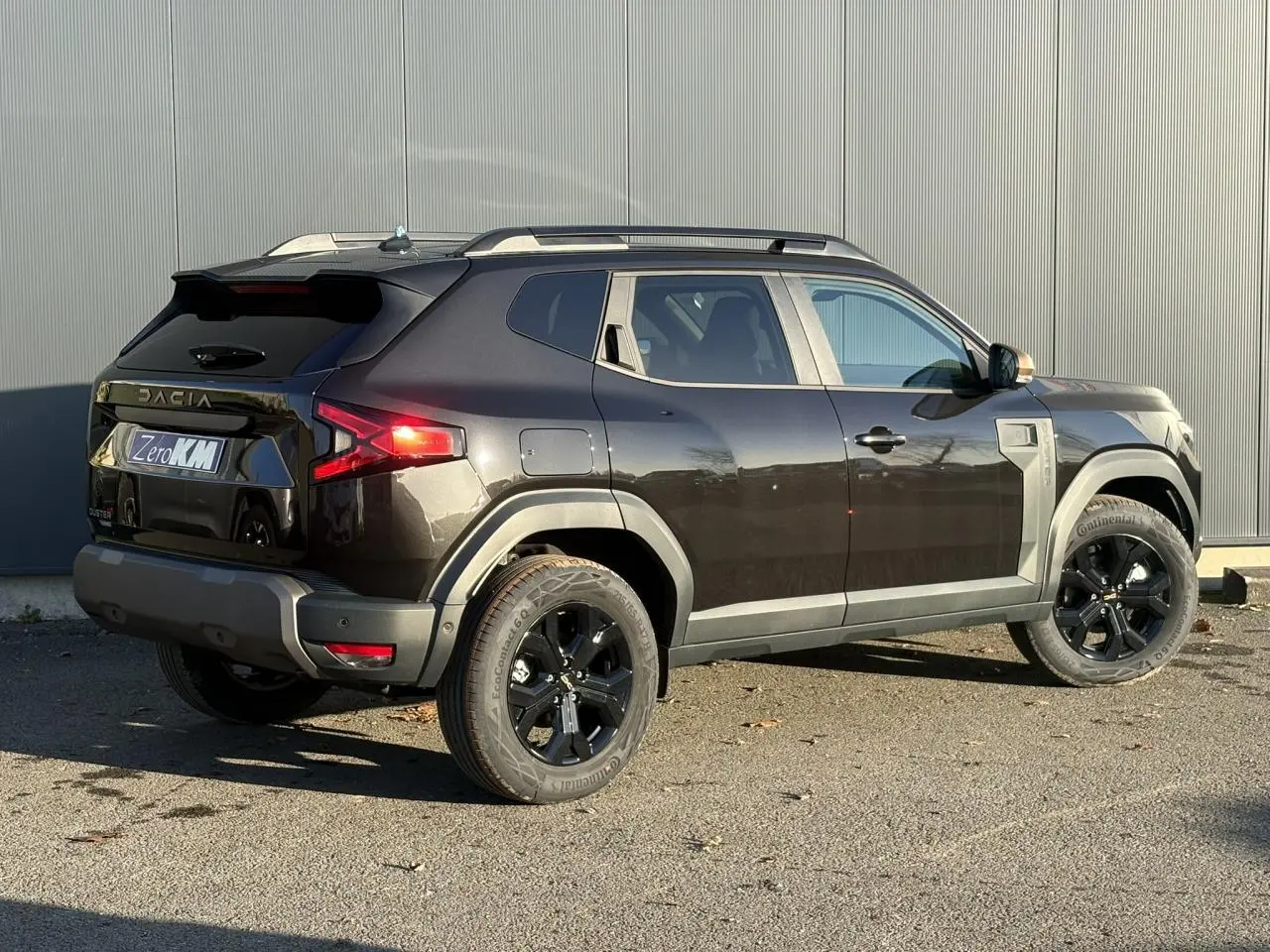 Vue 3/4 arrière droite du Dacia Duster 2026 noir nacré avec jantes alliage noires et barres de toit longitudinales.