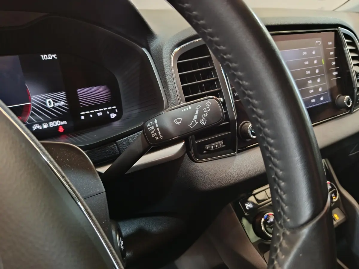 Gros plan sur le volant cuir et le combiné d'instruments numérique du Skoda Karoq blanc, version 2024, affichage multifonctions visible.