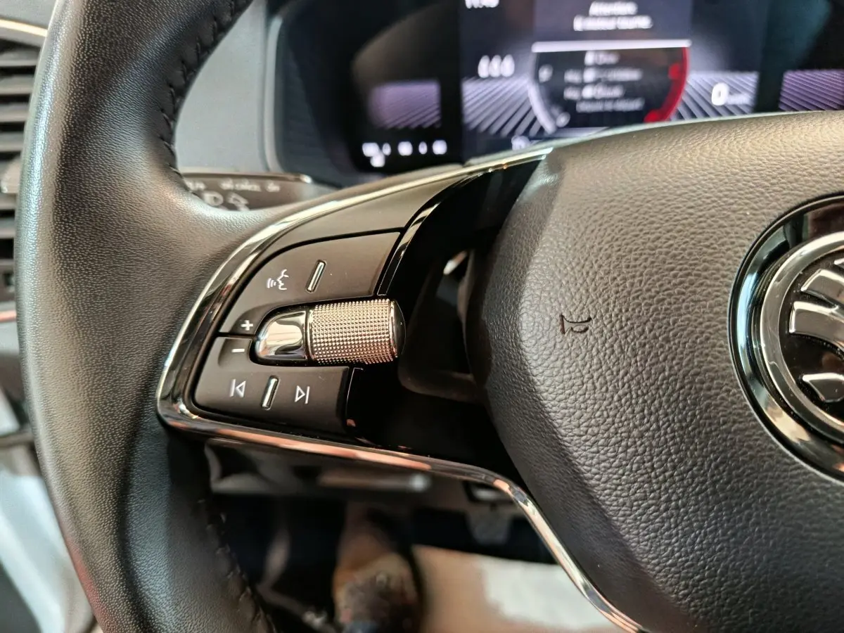 Gros plan sur la partie gauche du volant cuir noir du Skoda Karoq 2024, avec commandes intégrées et logo visible.