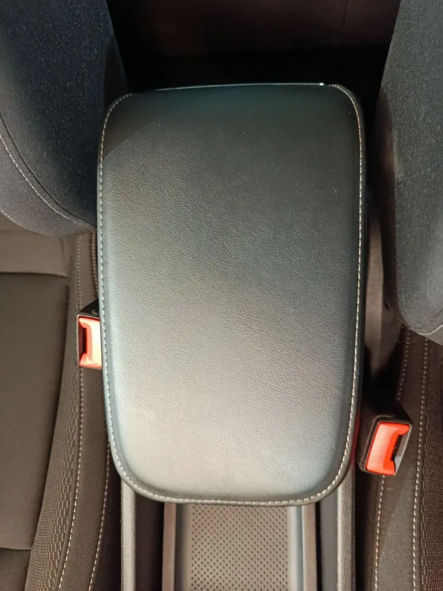 Vue rapprochée de l'accoudoir central noir en cuir et des ceintures de sécurité rouges du Skoda Karoq 2024.