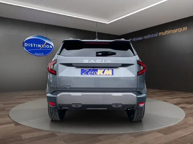 Vue arrière du Dacia Duster 1.6 Hybrid 140 gris schiste, avec feux LED et pare-chocs arrière robuste visible en intérieur showroom.