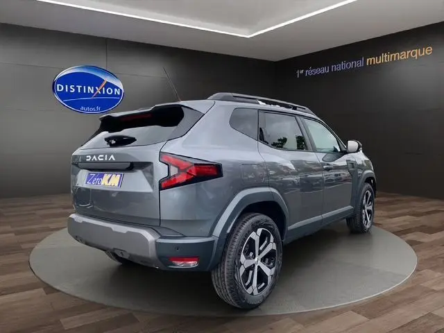 Vue 3/4 arrière droite du Dacia Duster 2025 gris schiste avec jantes alliage et toit noir contrasté.
