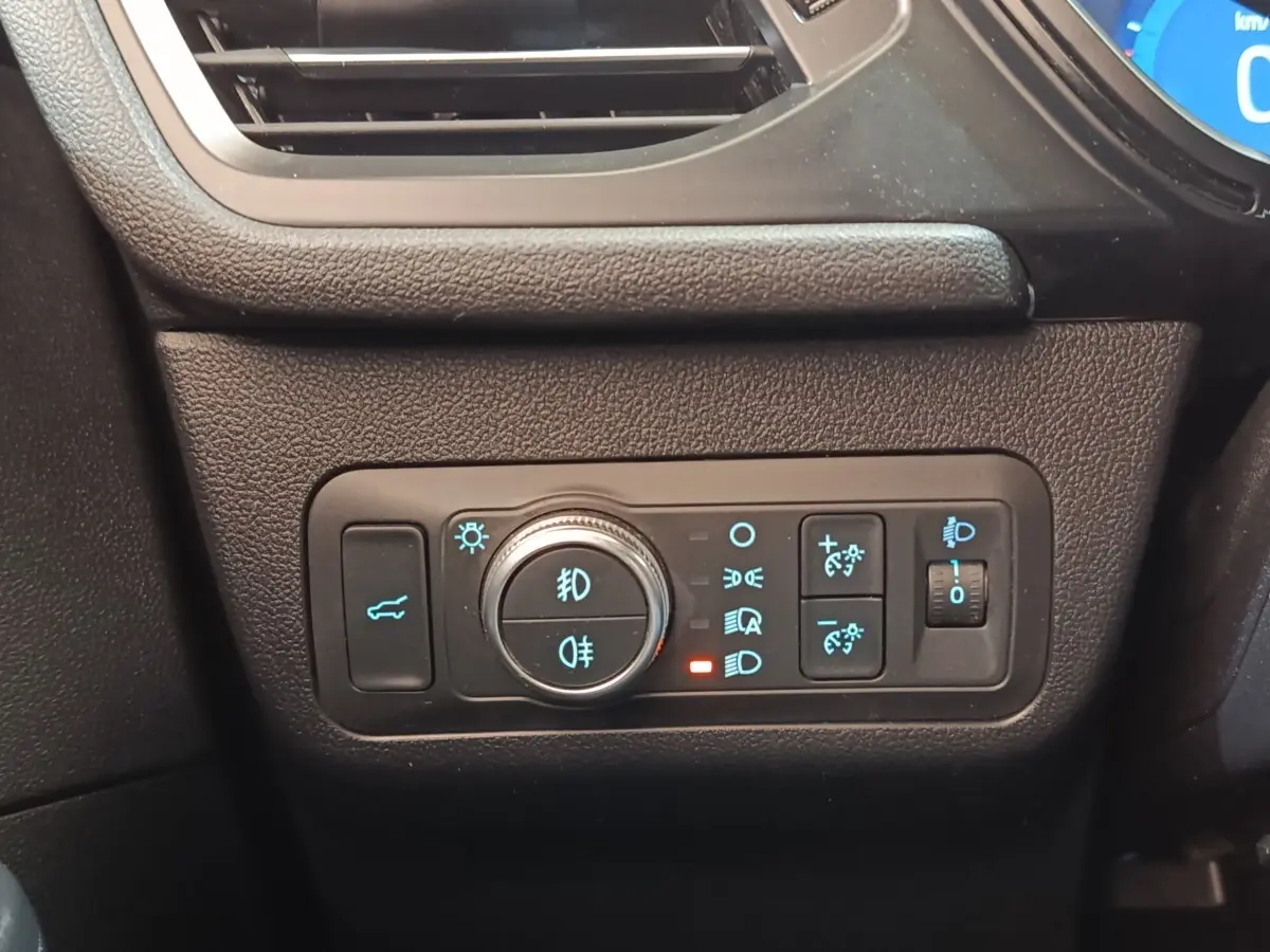 Vue rapprochée du panneau de commandes des feux et du coffre sur le côté gauche du tableau de bord noir du Ford Kuga gris foncé.