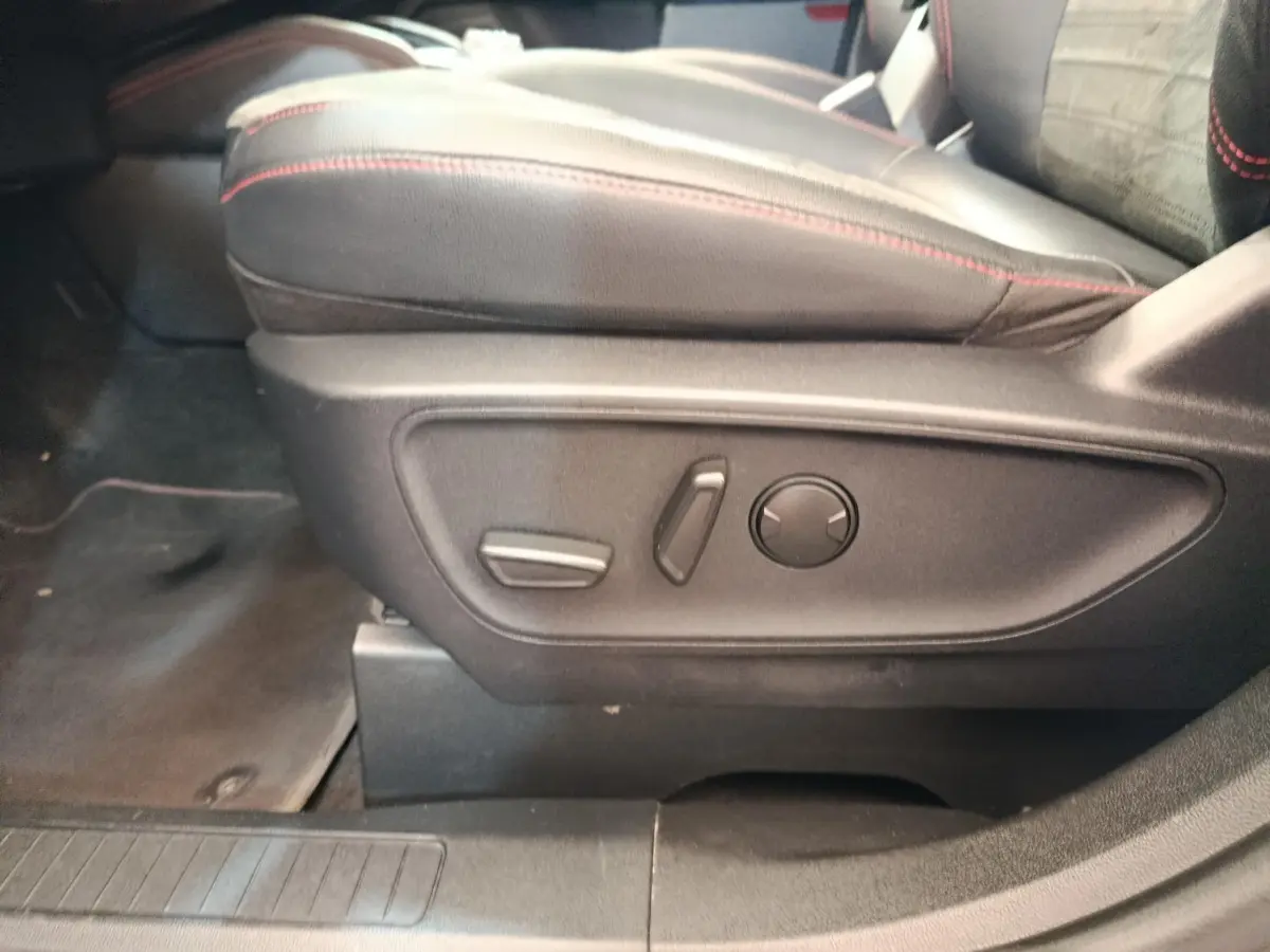 Détail des commandes électriques du siège avant droit en cuir noir avec surpiqûres rouges dans un Ford Kuga gris foncé 2023.