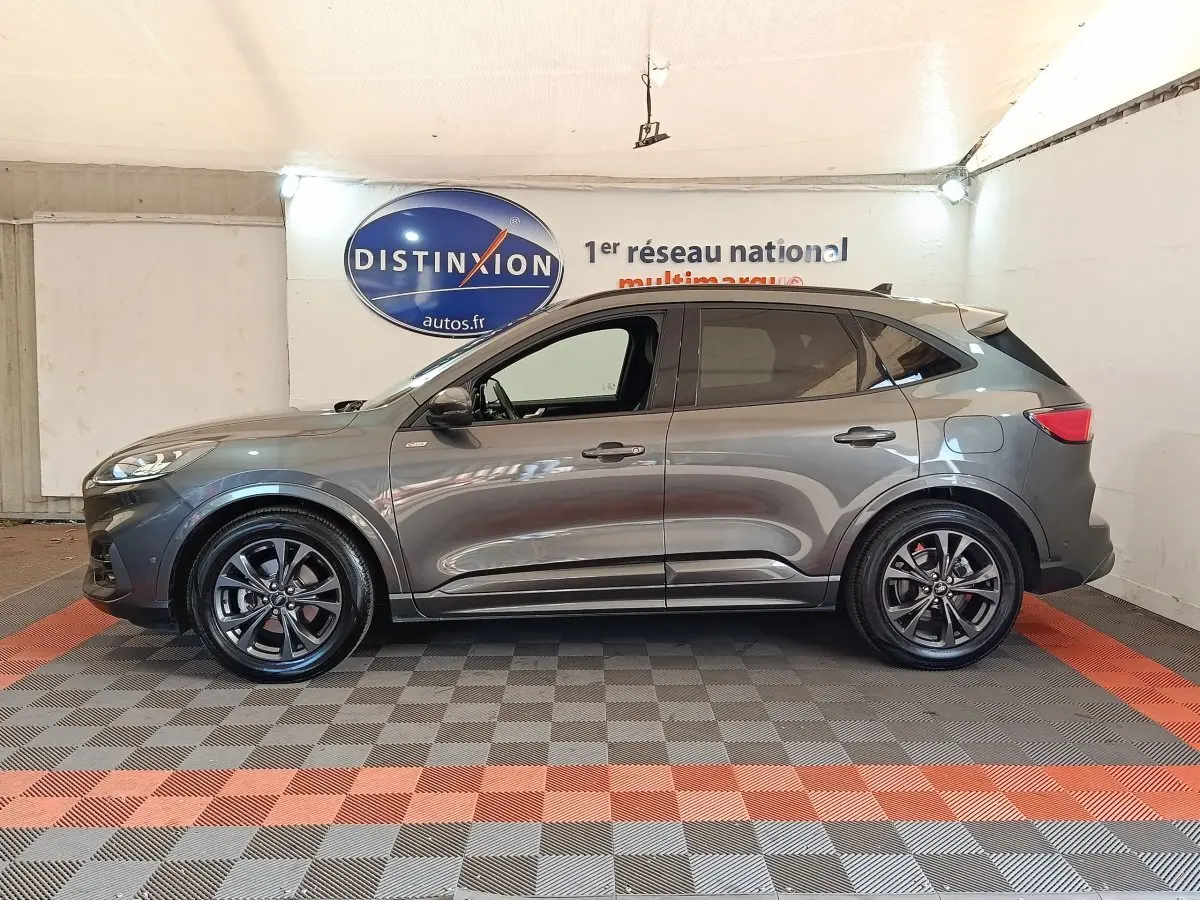 Vue de profil côté gauche d’un Ford Kuga gris foncé ST-Line X avec jantes noires dans un showroom intérieur.