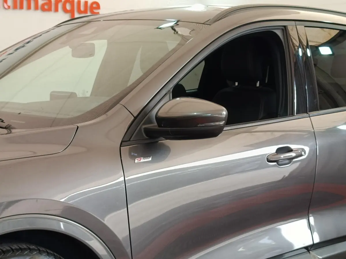 Vue latérale gauche rapprochée du Ford Kuga gris foncé avec badge ST-Line X sur l'aile avant.