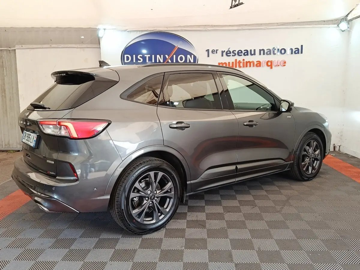 Ford Kuga gris foncé vu en 3/4 arrière droit, avec jantes noires et toit noir brillant dans un showroom.