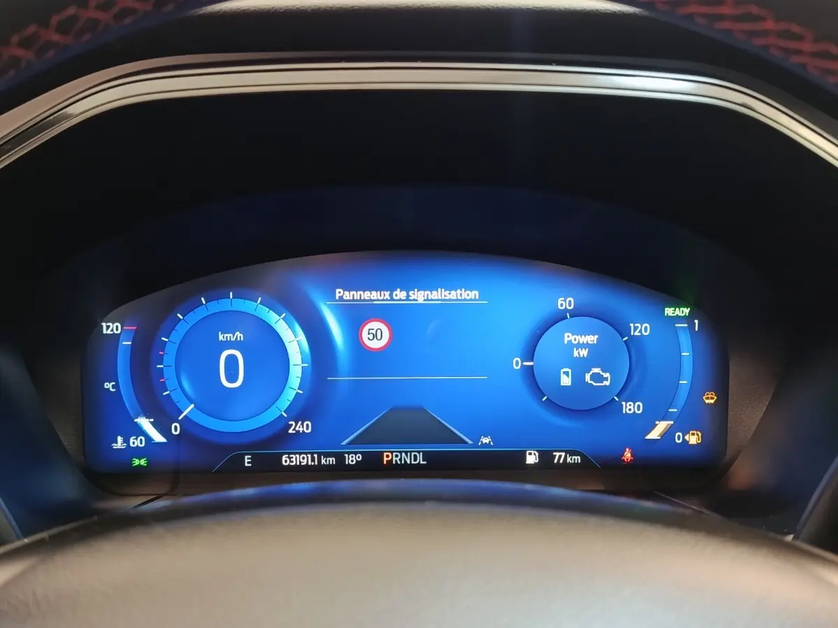 Vue du combiné d'instruments numérique bleu du Ford Kuga 2023, affichant vitesse, puissance et panneaux de signalisation.