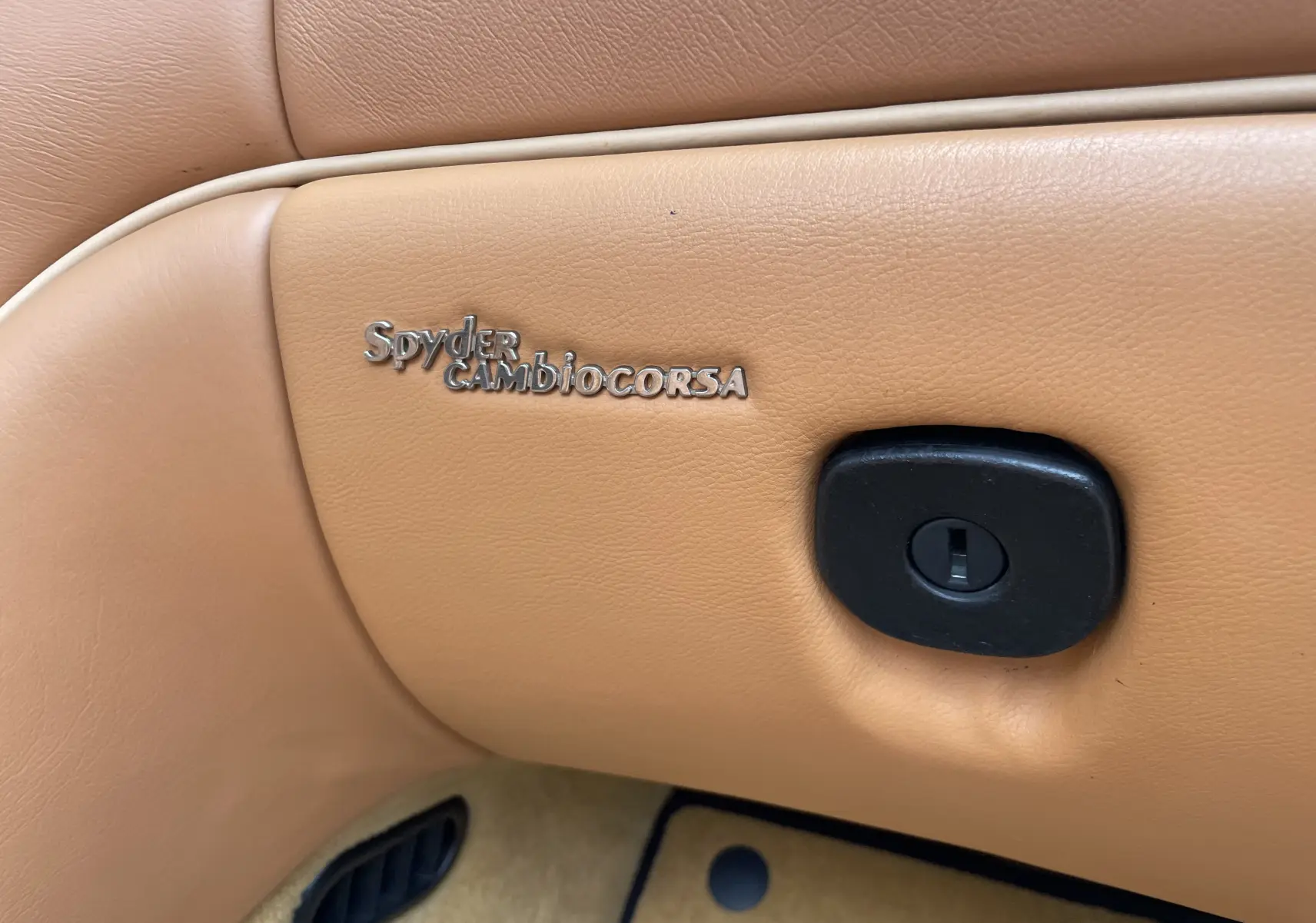 Gros plan sur le badge Spyder Cambiocorsa incrusté dans le cuir beige de l’habitacle d’une Maserati Spyder 2002.