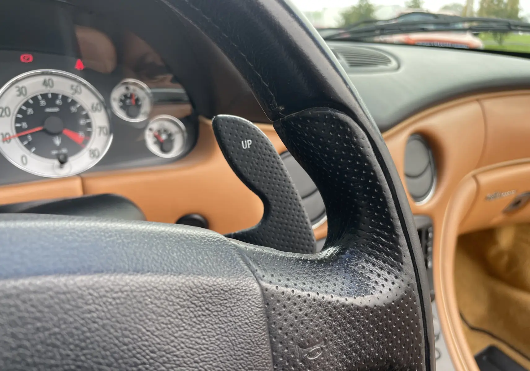 Gros plan sur le volant perforé et les palettes de vitesse d'une Maserati Spyder gris Nuvolari, tableau de bord cuir camel visible.