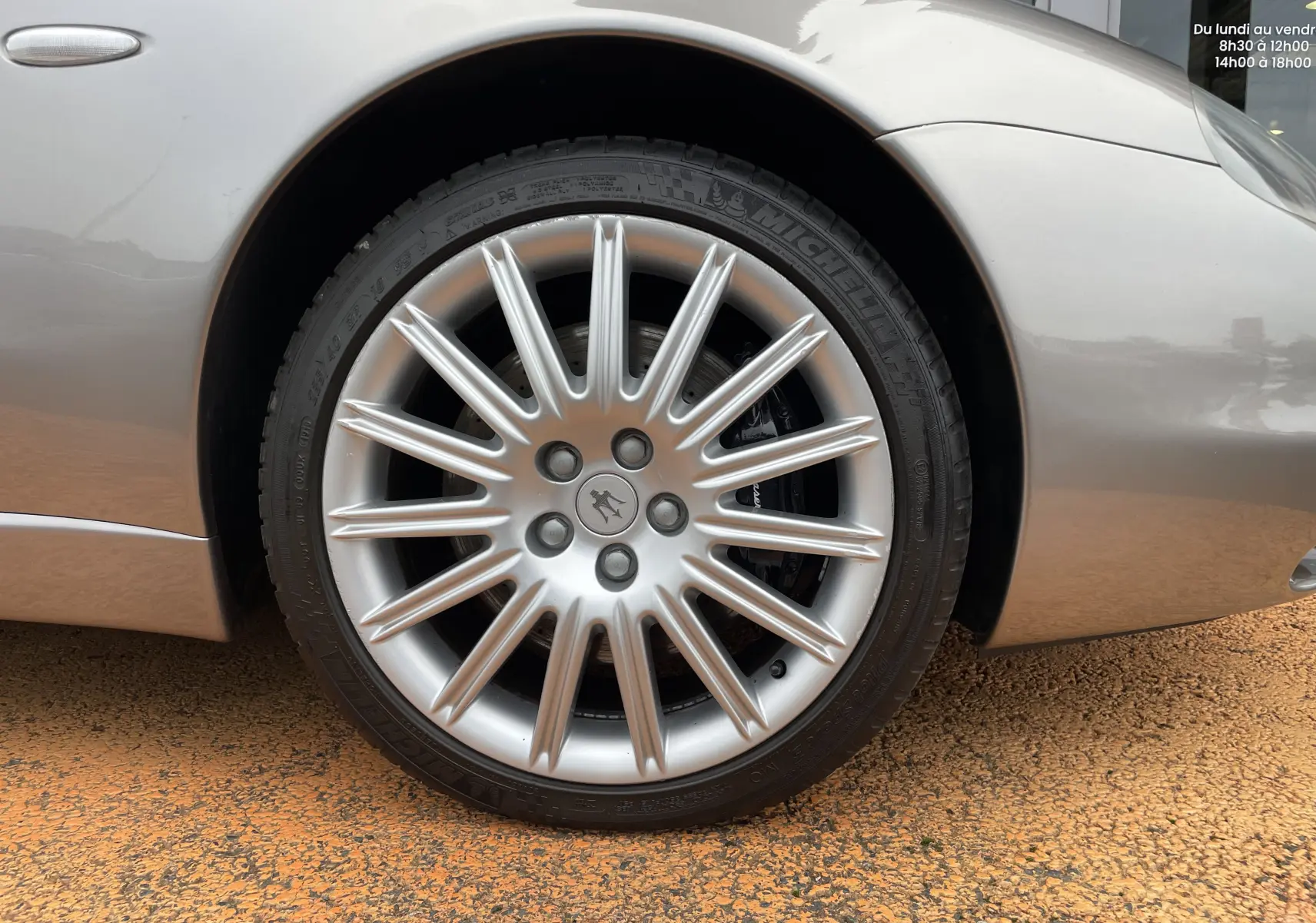 Gros plan sur la roue avant gauche gris nuvolari d'une Maserati Spyder 2002 avec jante argentée à multiples branches.