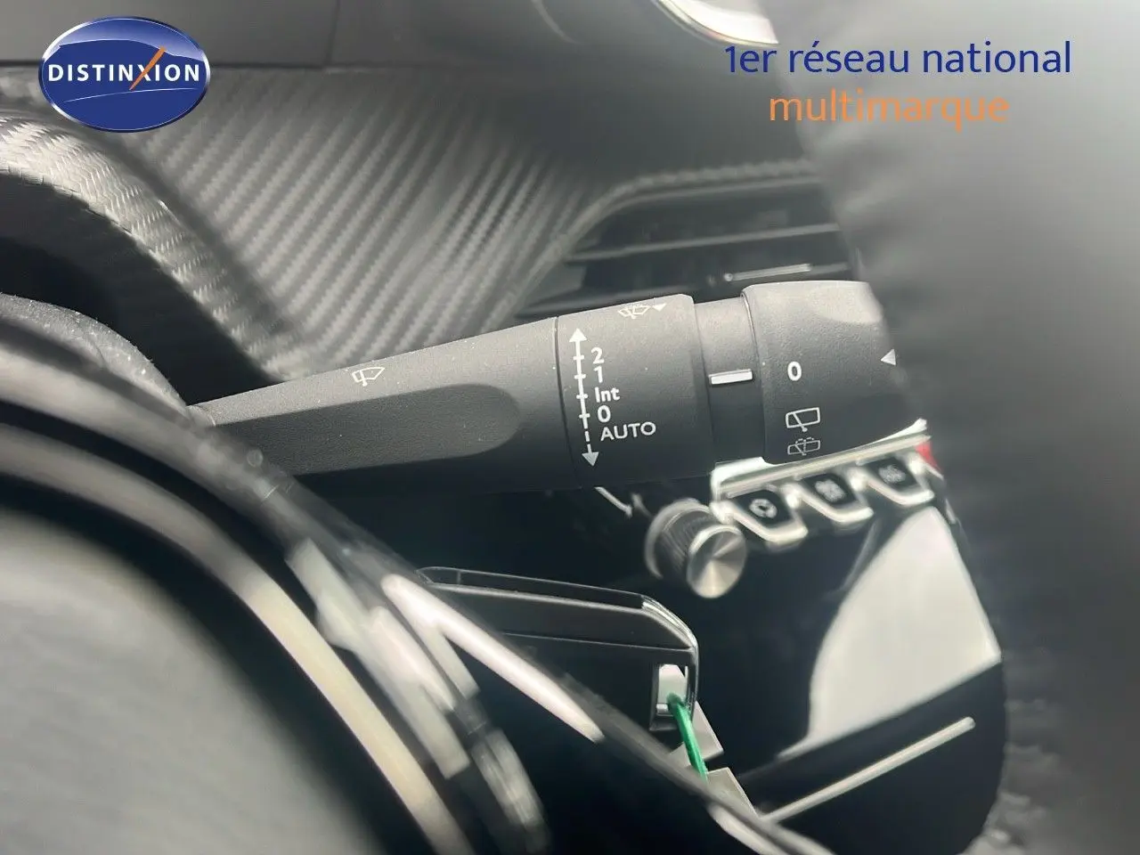 Gros plan sur le commodo d'essuie-glace à gauche du volant dans l'habitacle d'une Peugeot 2008 blanche.