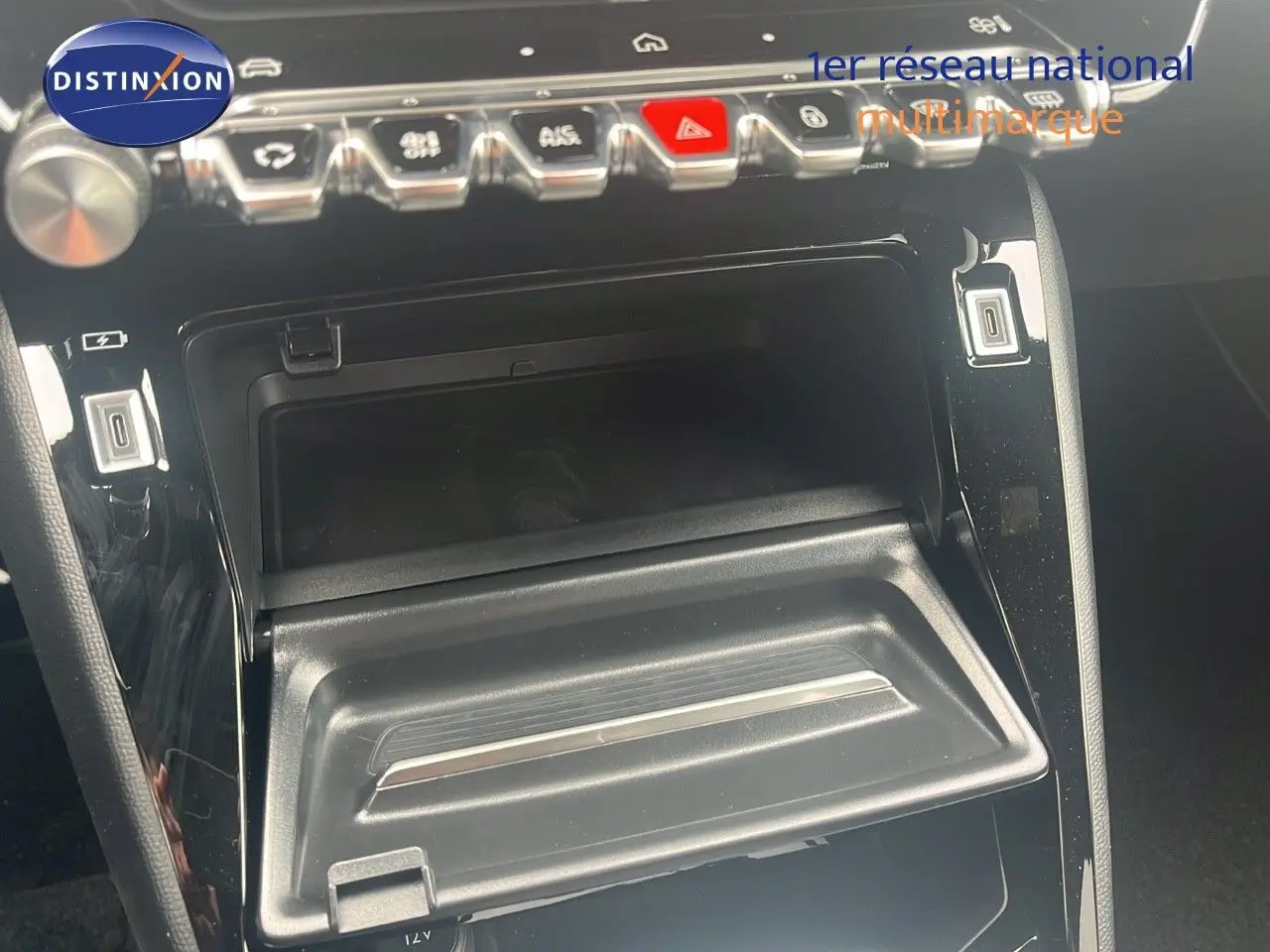 Intérieur de la Peugeot 2008 2025, vue rapprochée de la console centrale avec commandes et rangement ouvert noir brillant.