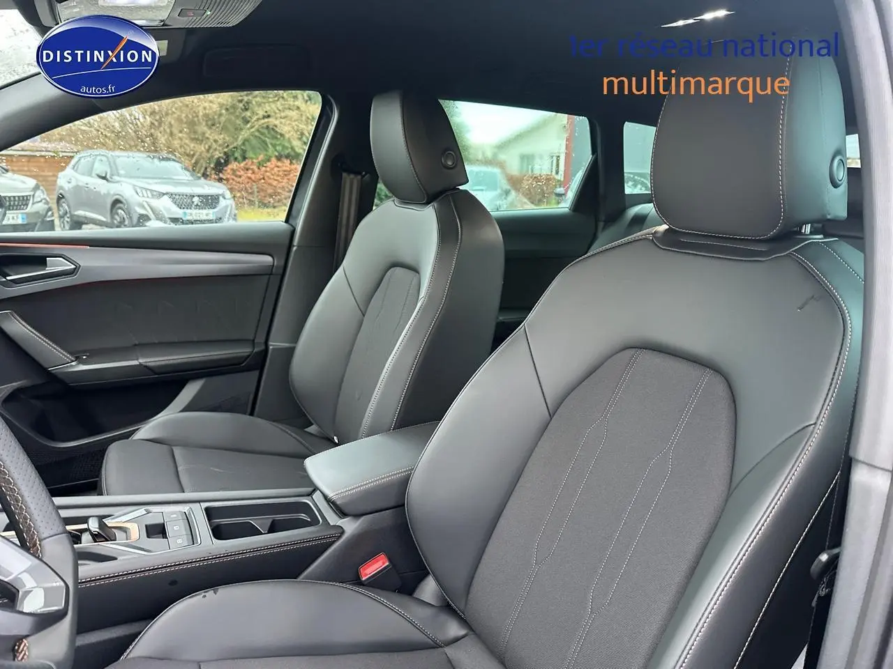 Vue intérieure de face des sièges avant en cuir gris foncé de la CUPRA LEON ST 1.5 etsi hybrid 2025 avec accoudoir central.