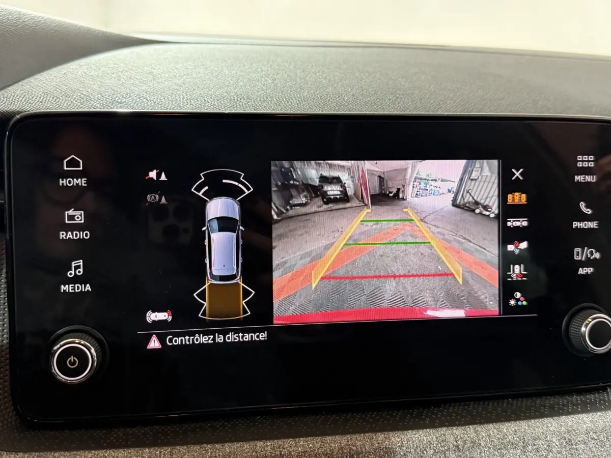 Écran tactile central du Skoda Kamiq rouge 2024 montrant la caméra de recul et les capteurs de stationnement.