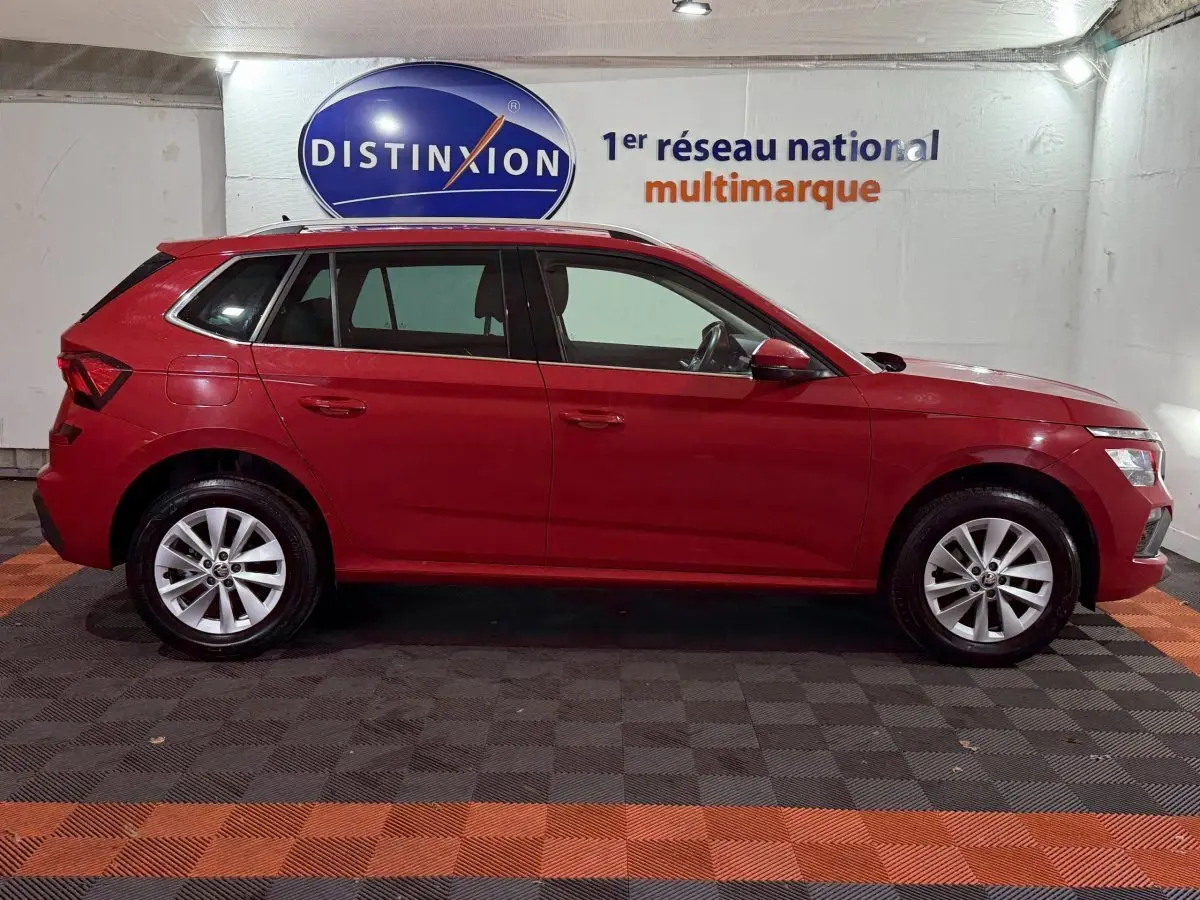 Profil latéral droit d'un Skoda Kamiq rouge 2024, avec jantes alliage et barres de toit noires visibles.
