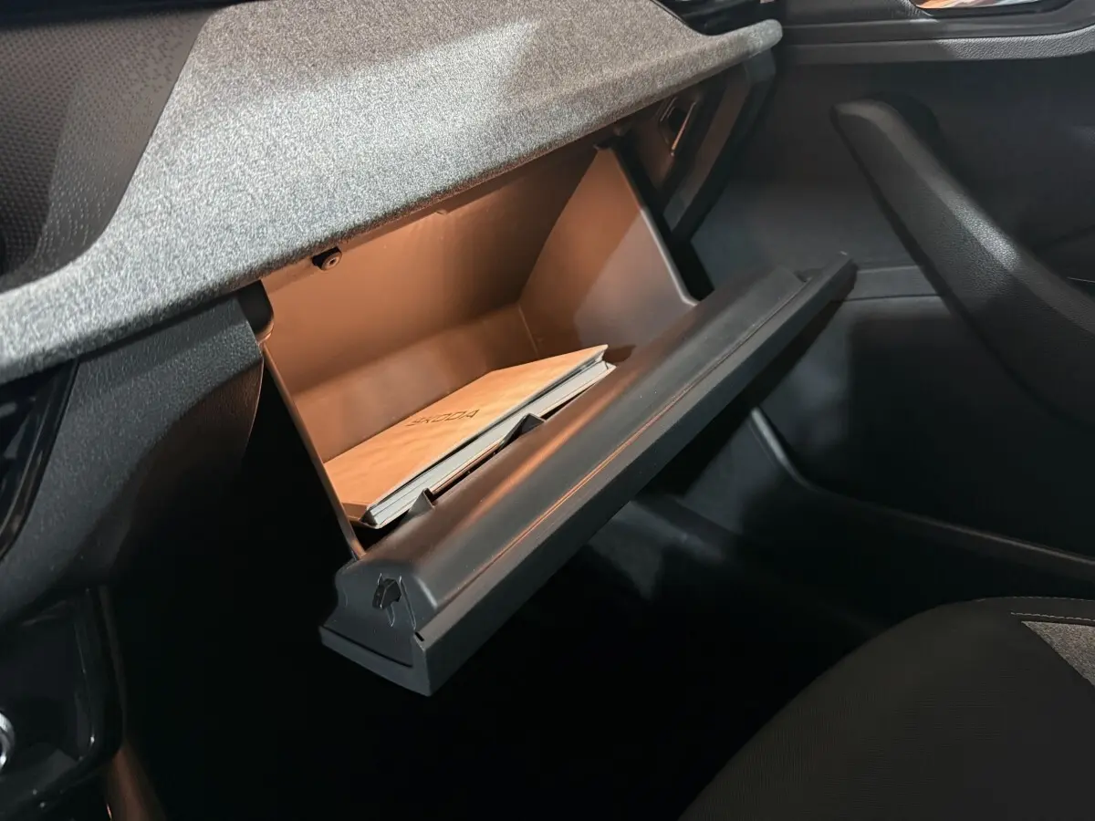 Gros plan sur la boîte à gants ouverte du Skoda Kamiq 2024, montrant un manuel à l'intérieur, intérieur noir.