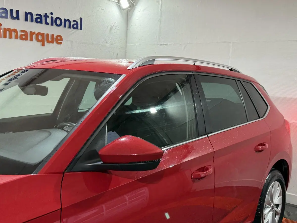 Vue de côté gauche du SKODA KAMIQ rouge 2024, mettant en valeur les vitres teintées et les barres de toit argentées.