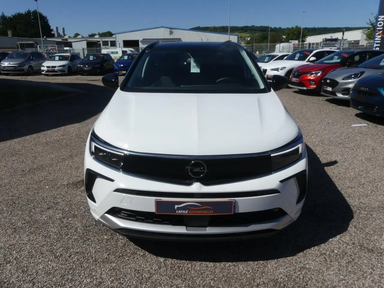 Vue avant d'un Opel Grandland blanc métallisé avec calandre noire brillante sur un parking extérieur.