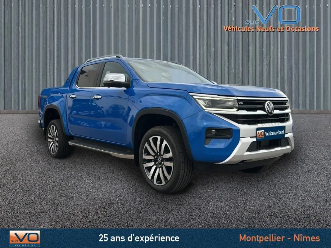 Vue 3/4 avant gauche d’un Volkswagen Amarok bleu 2025 avec jantes alliage 21 pouces et marchepieds visibles.