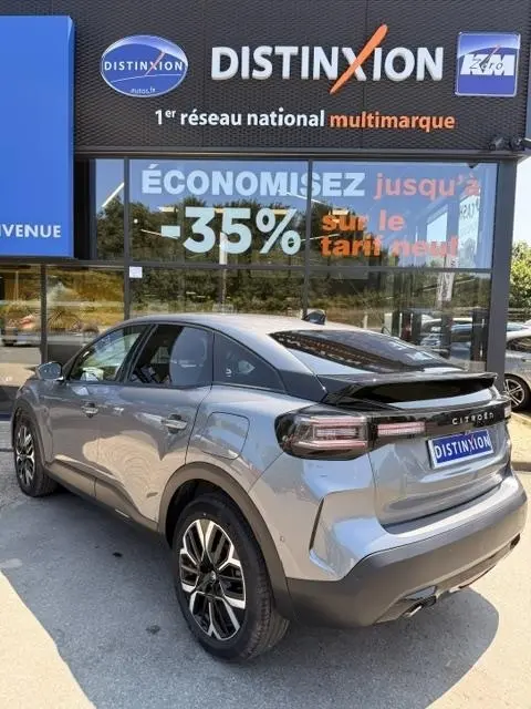 Vue 3/4 arrière droite d'une Citroën C4 gris foncé 2025 avec spoiler de coffre et jantes alliage noires.