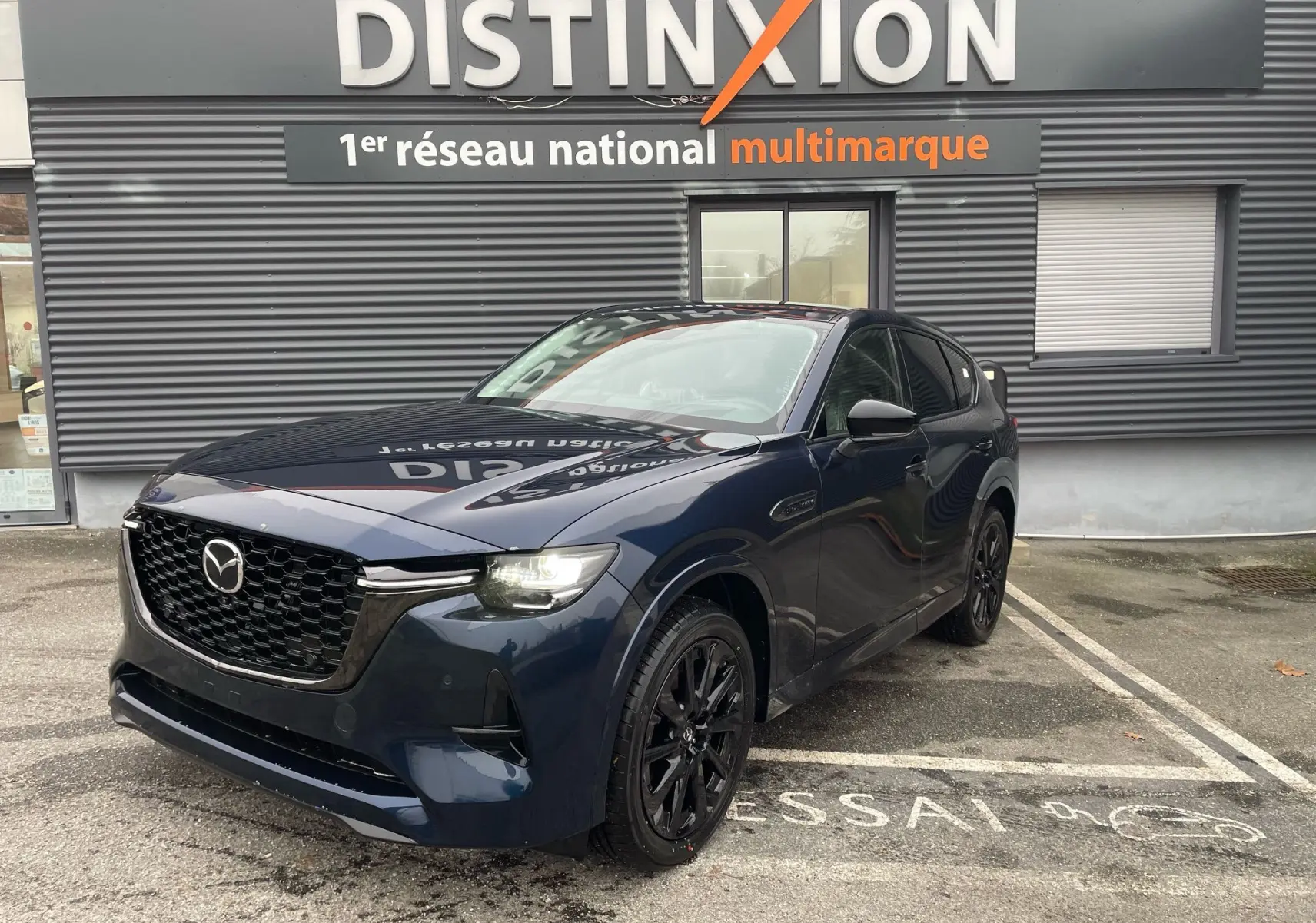 Mazda CX-60 Deep Crystal Blue en 3/4 avant droit, avec calandre noire et jantes noires brillantes, stationné devant un bâtiment.