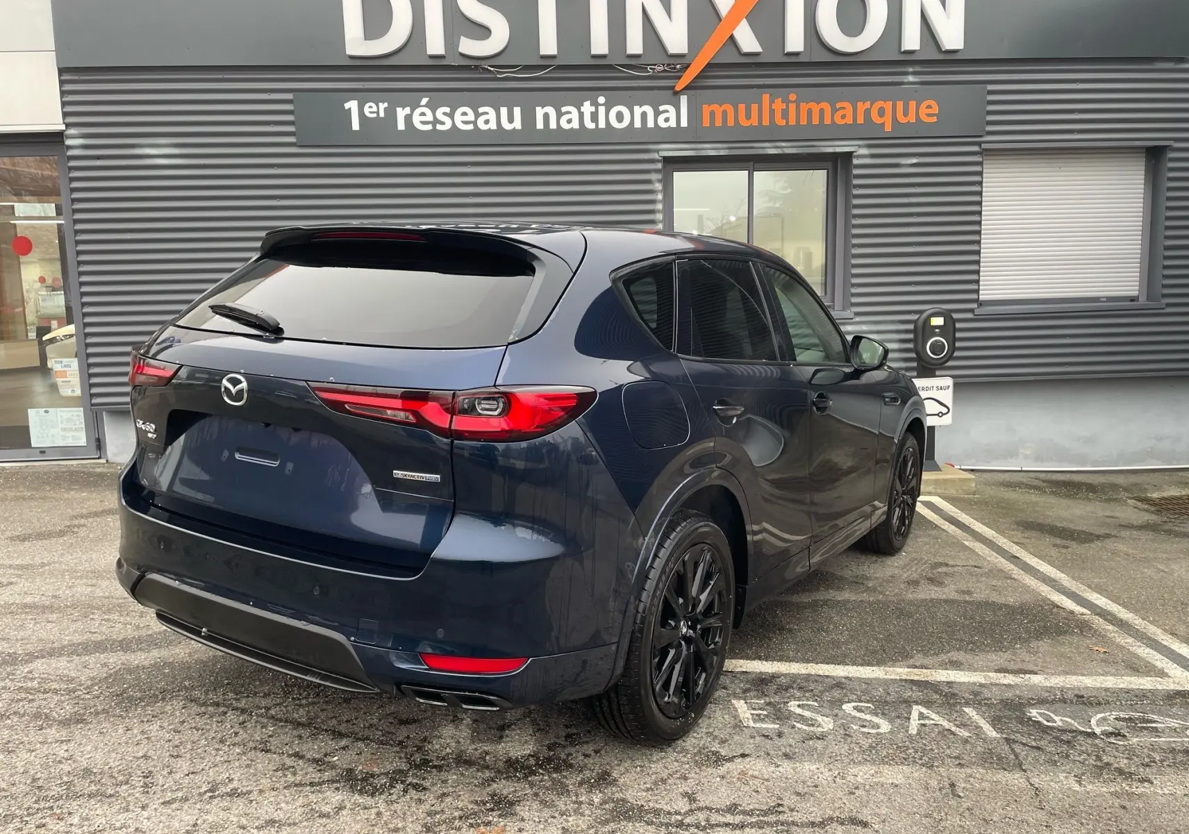 Vue 3/4 arrière droite du Mazda CX-60 Deep Crystal Blue avec jantes noires, stationné devant un concessionnaire Distinxion.