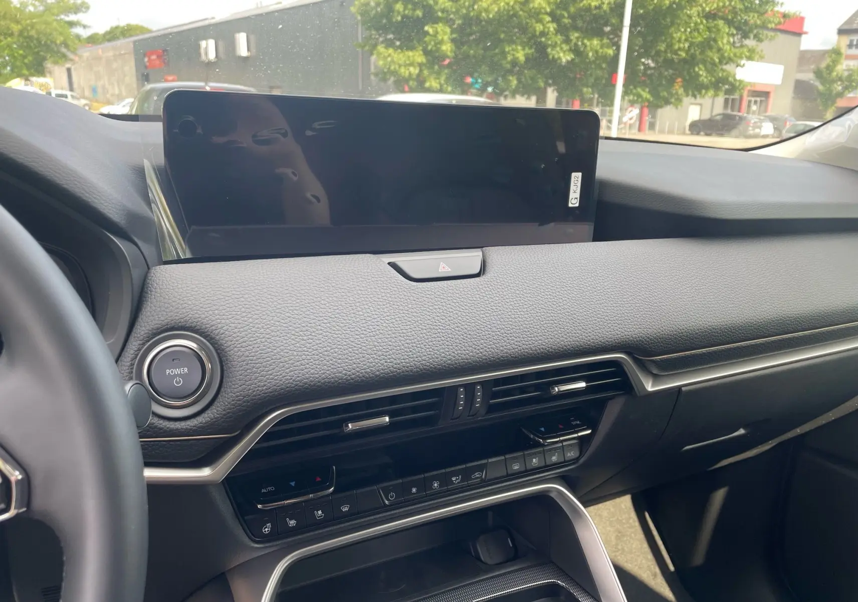 Tableau de bord noir du Mazda CX-60 2024 avec écran tactile large et commandes climatisation visibles côté passager.