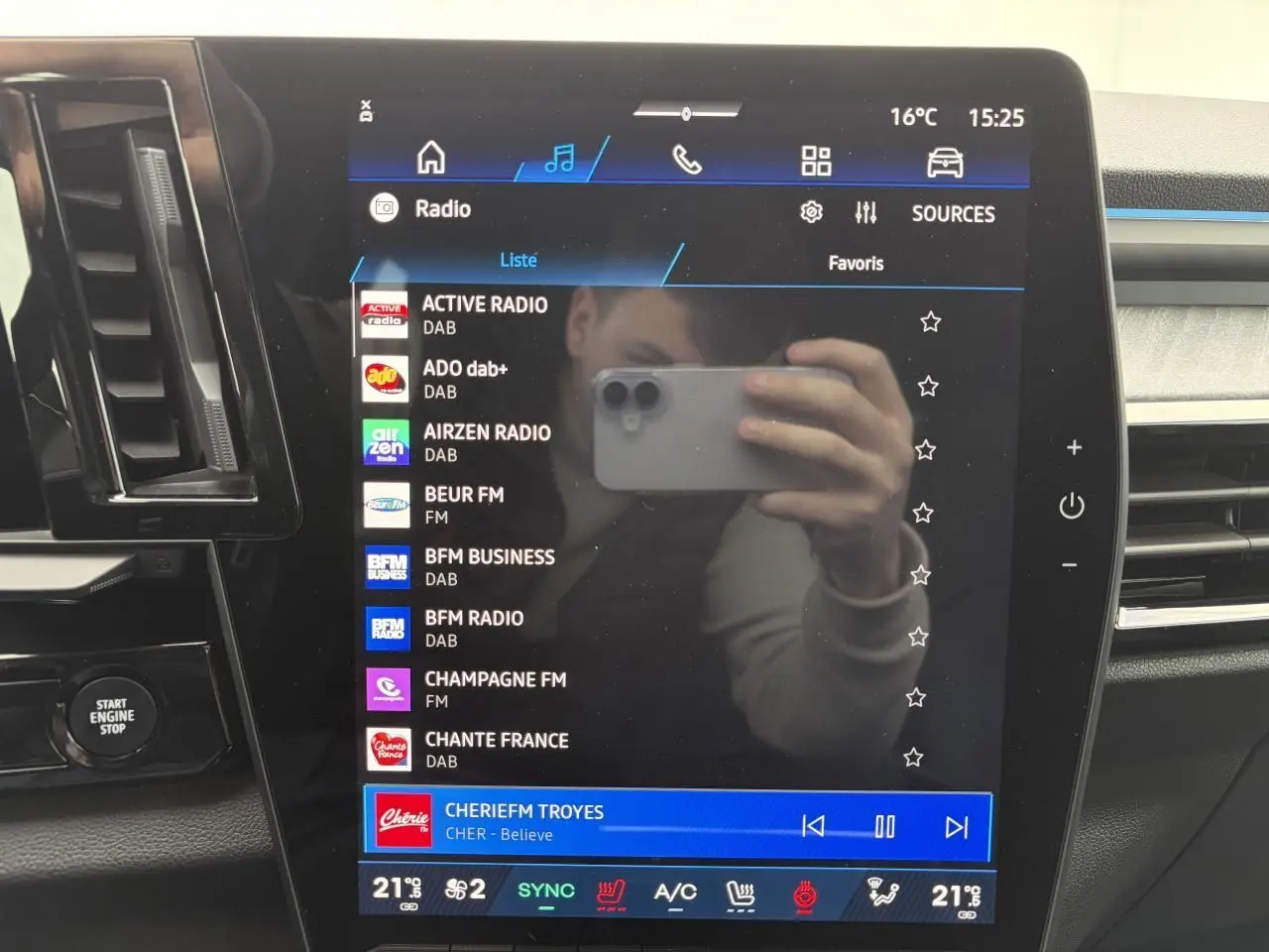 Écran central tactile du tableau de bord Renault Rafale 2025 affichant les stations radio, avec reflets et commandes autour.