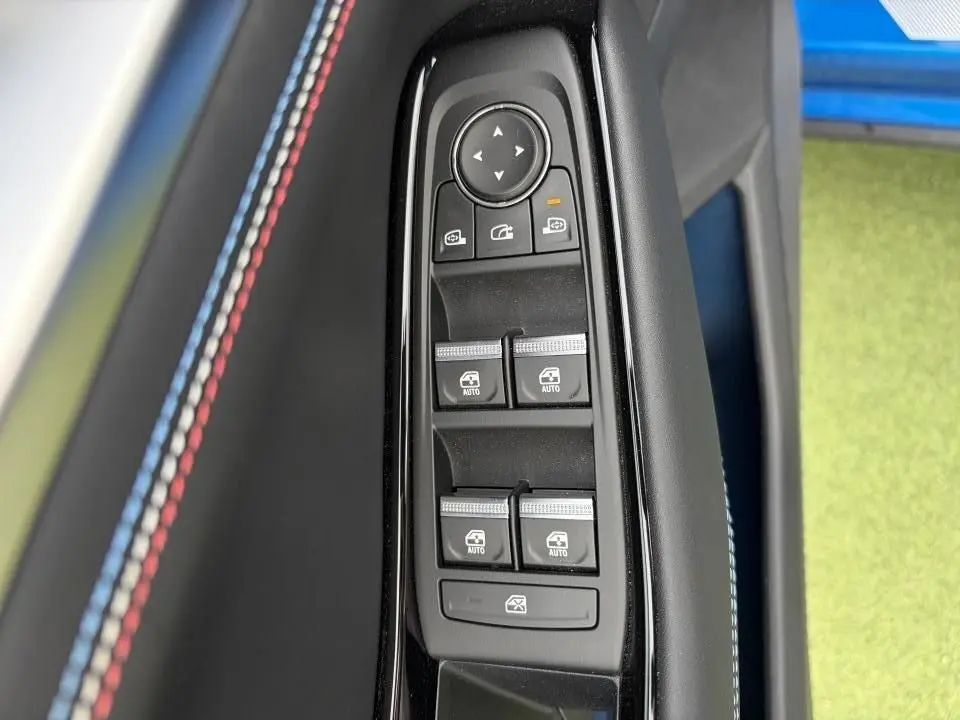 Gros plan sur les commandes de vitres et rétroviseurs avec surpiqûres tricolores sur la garniture intérieure bleu sommet.