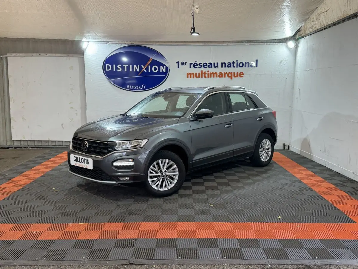 Volkswagen T-Roc gris foncé vue 3/4 avant droit dans un showroom avec sol noir et bandes orange.