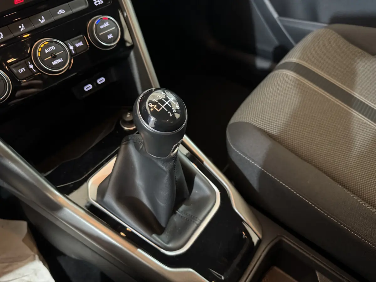 Gros plan sur levier de vitesses manuel et console centrale noire du Volkswagen T-Roc gris foncé, siège tissu à motifs visible à droite.