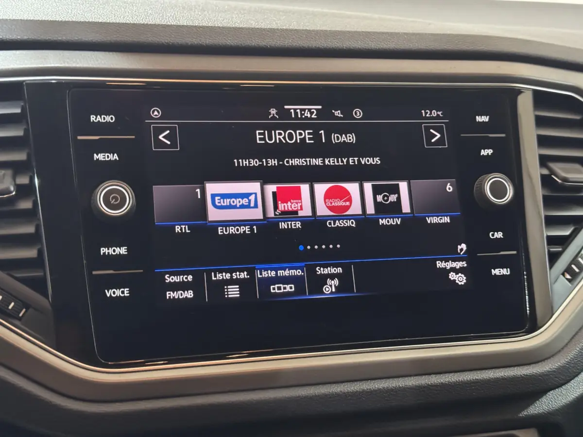 Écran tactile central du tableau de bord du Volkswagen T-Roc 2.0 TDI gris foncé, affichant les stations radio FM/DAB.
