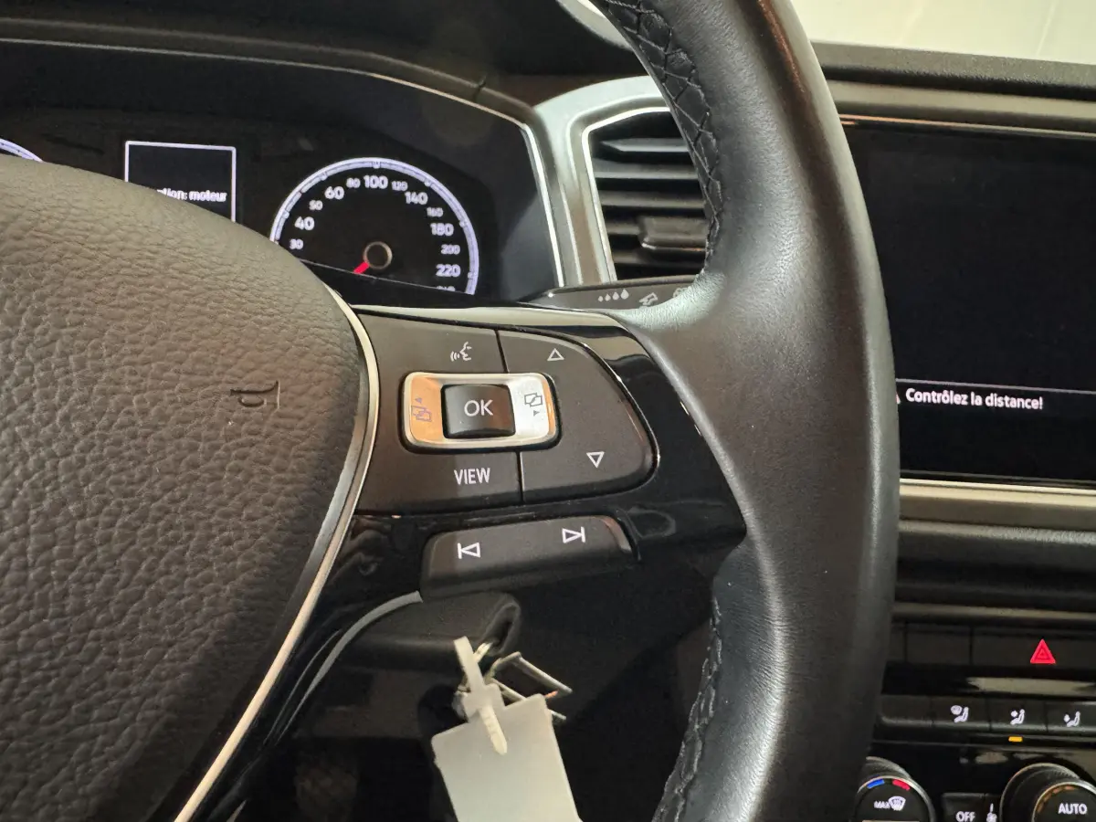 Gros plan sur le volant cuir noir et le tableau de bord digital du Volkswagen T-Roc gris foncé 2021, version Lounge Business.