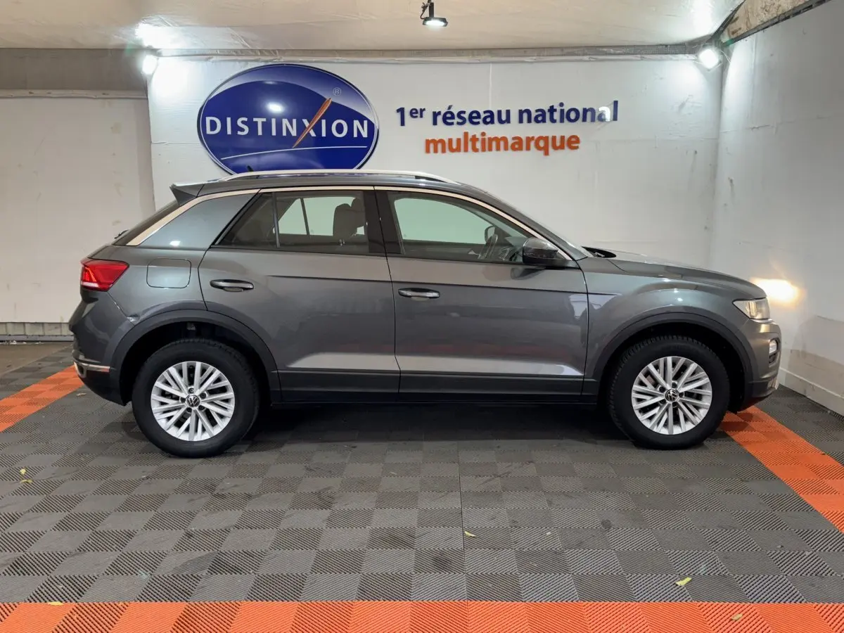 Profil côté gauche d'un Volkswagen T-Roc gris foncé 2021 garé en intérieur avec jantes alliage et rails de toit noirs.