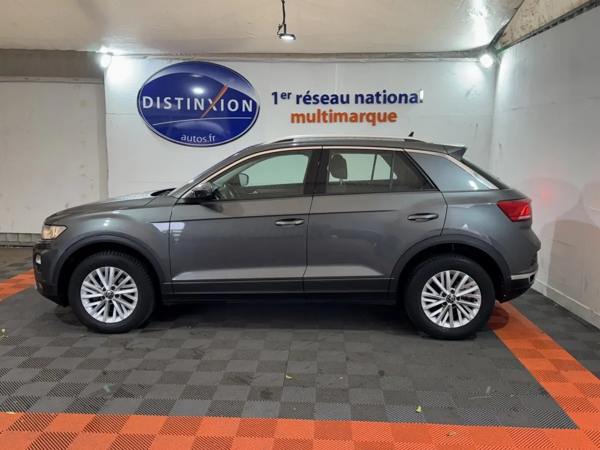 Profil côté gauche d'un Volkswagen T-Roc gris foncé 2021 garé en intérieur avec jantes alliage et toit noir.