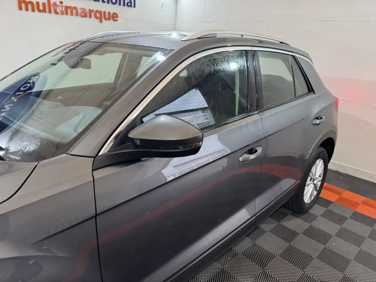 Vue latérale côté gauche du Volkswagen T-Roc gris foncé avec rétroviseur et jante alliage visibles en intérieur showroom.