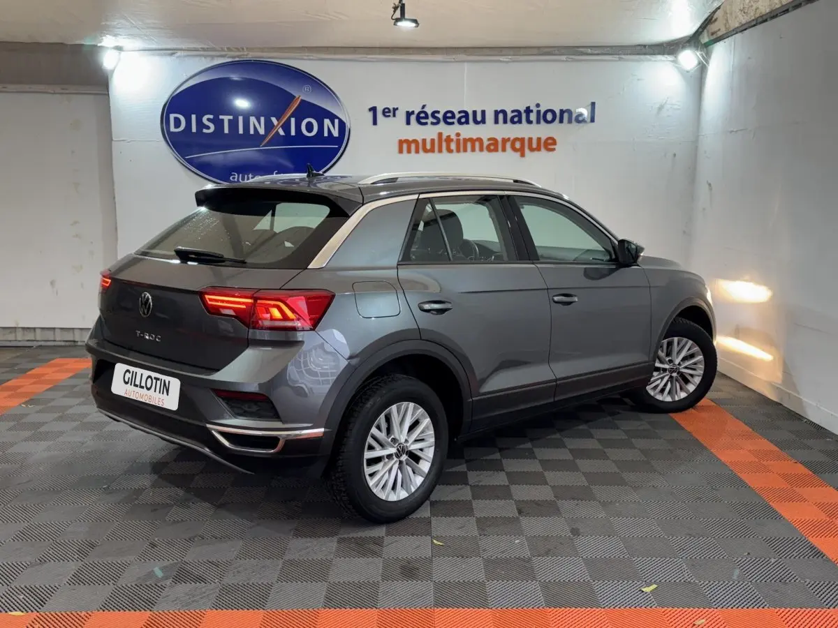 Volkswagen T-Roc gris foncé en 3/4 arrière droit, feux arrière allumés et jantes alliage visibles.