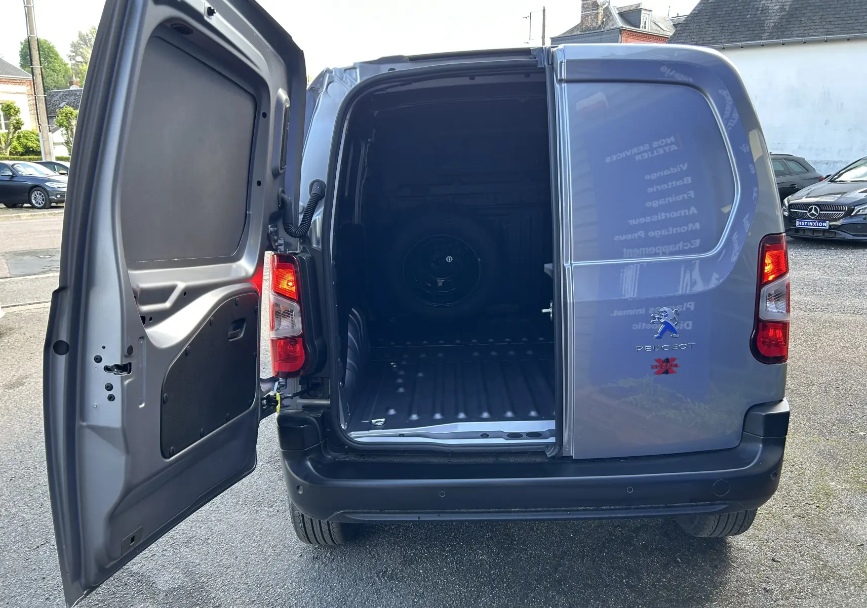 Vue arrière du Peugeot Partner Dangel gris Artense avec porte gauche ouverte montrant l'espace de chargement vide.